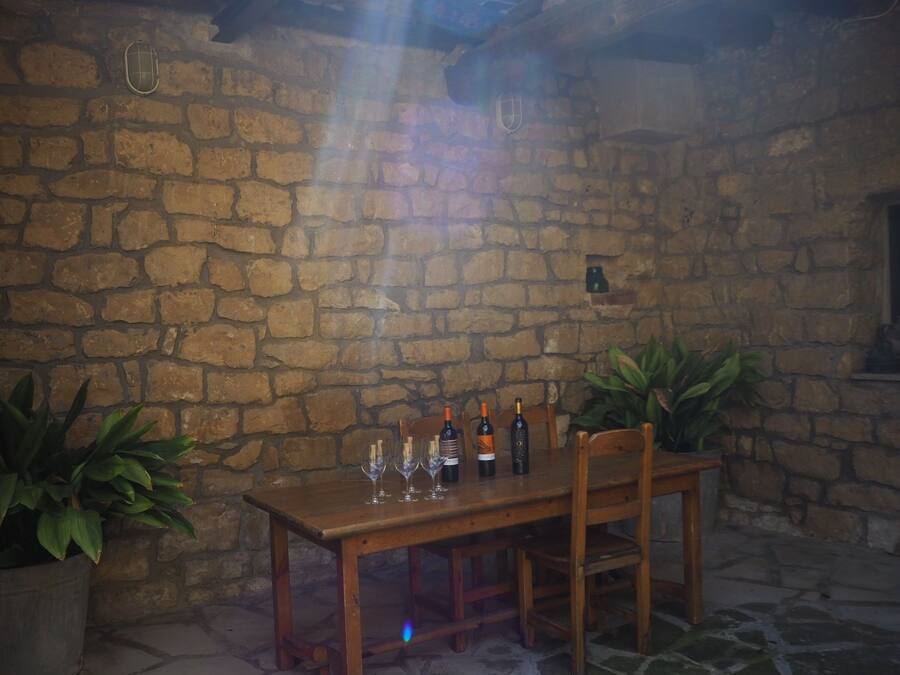 Habitación con paredes de piedra y una mesa de madera dispuesta para comer, con botellas de vino y copas.