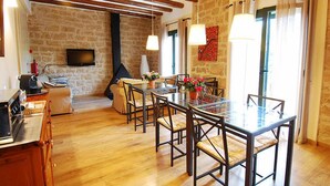 A dining area with a glass table and chairs, a stone wall, and a television mounted on the wall. - Vilosell Wine Hotel (El Vilosell)