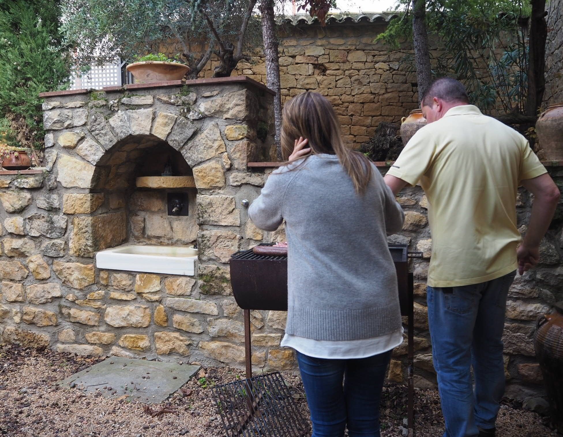 A stone-built outdoor oven with a brick shelf, a white sink, and a grill.