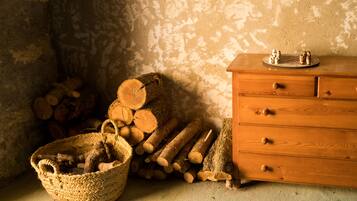 Une pièce rustique avec une commode en bois, un panier tressé rempli de bûches et une pile de bois de chauffage adossée à un mur à la texture particulière.