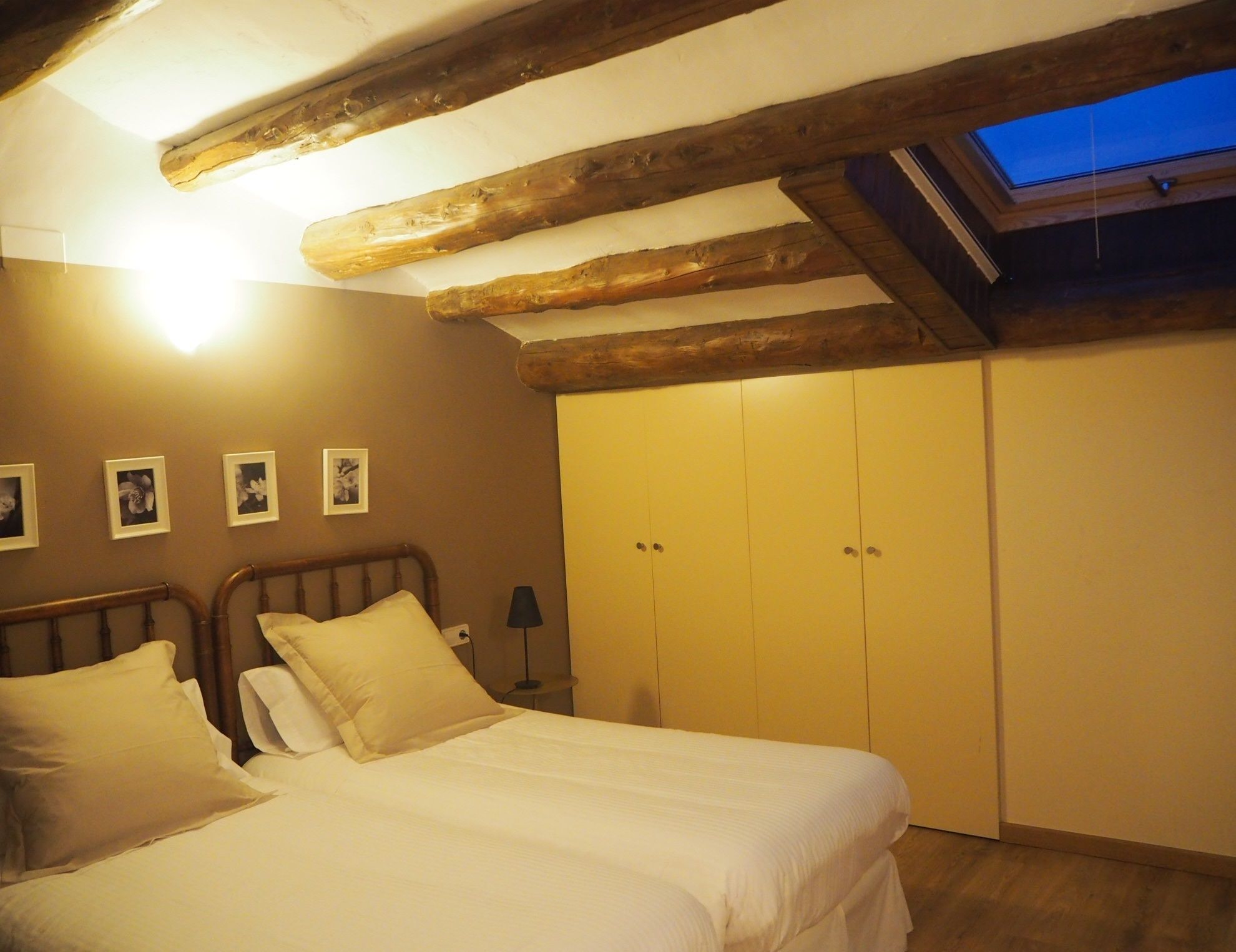 A bedroom with a bed, wooden beams, a skylight, and a wardrobe.