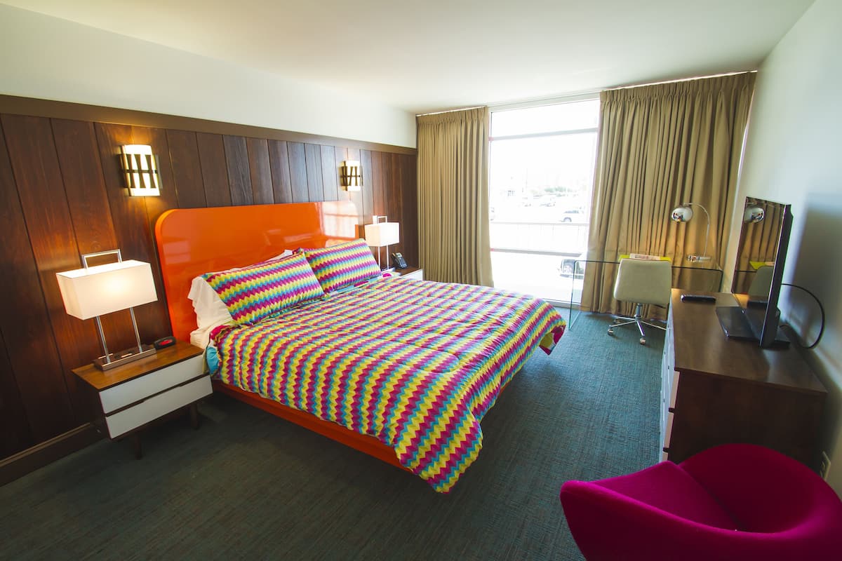 A hotel room with a large bed, a desk with a computer, a chair, and a window with curtains.