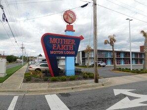 A sign for Mother Earth Motor Lodge with a parking lot and a building in the background. - Mother Earth Motor Lodge (Kinston)