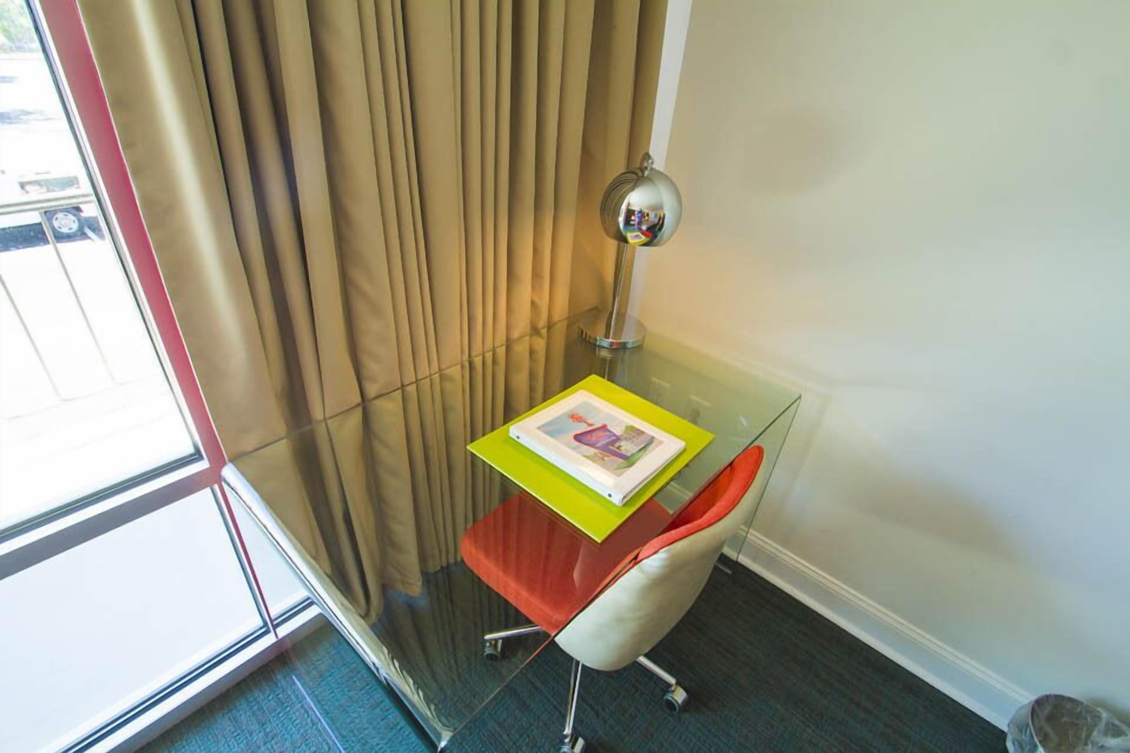 Un bureau d’angle avec un bureau en verre, une lampe et une chaise.