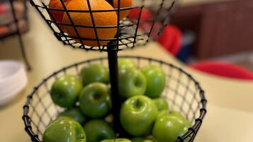 A kitchen counter with a fruit basket containing green apples and oranges.