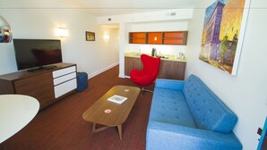 A modern living room with a TV, sofa, coffee table, and a red chair. - Mother Earth Motor Lodge (Kinston)