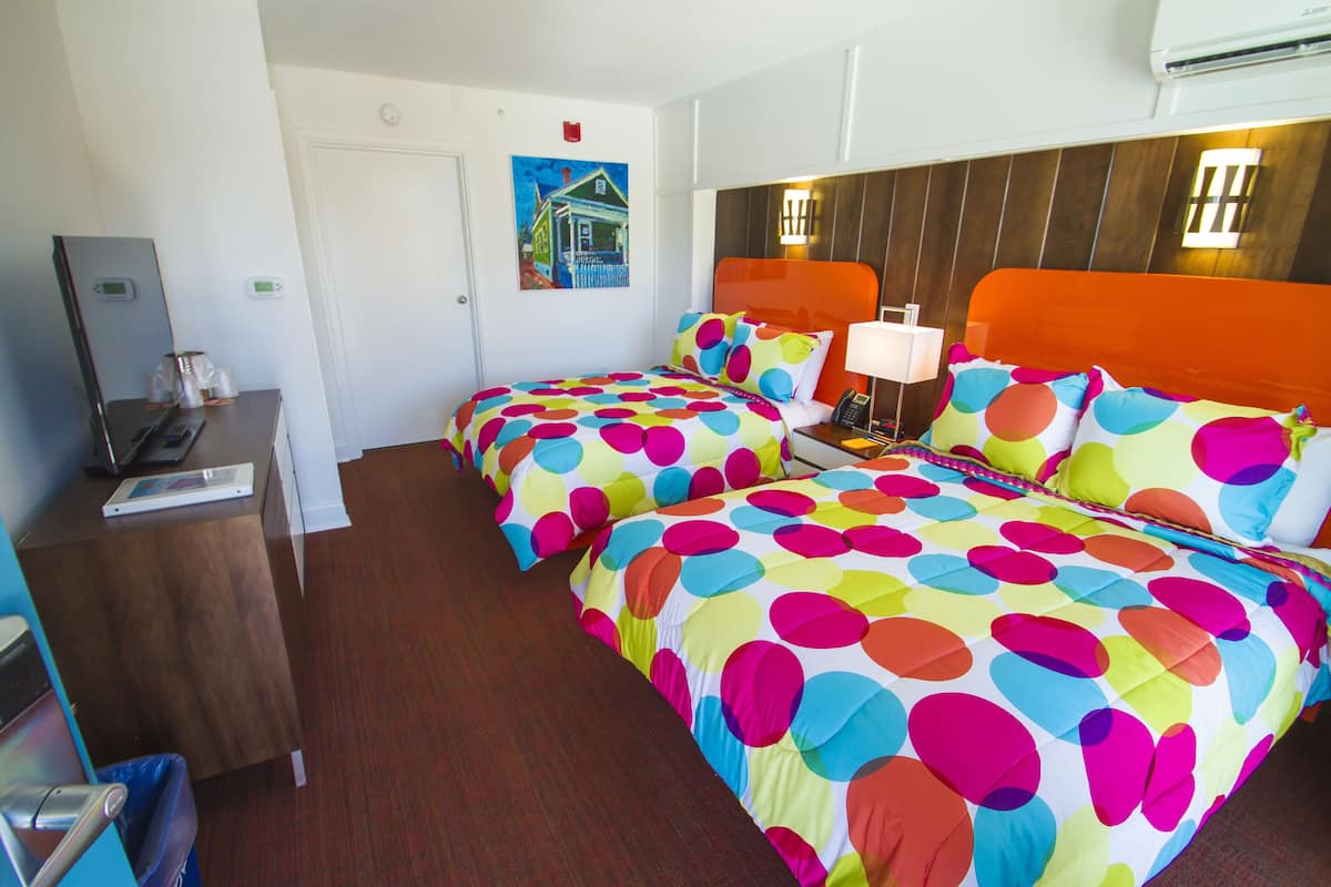 A hotel room with two beds, a desk with a computer, a trash bin, and a painting on the wall.