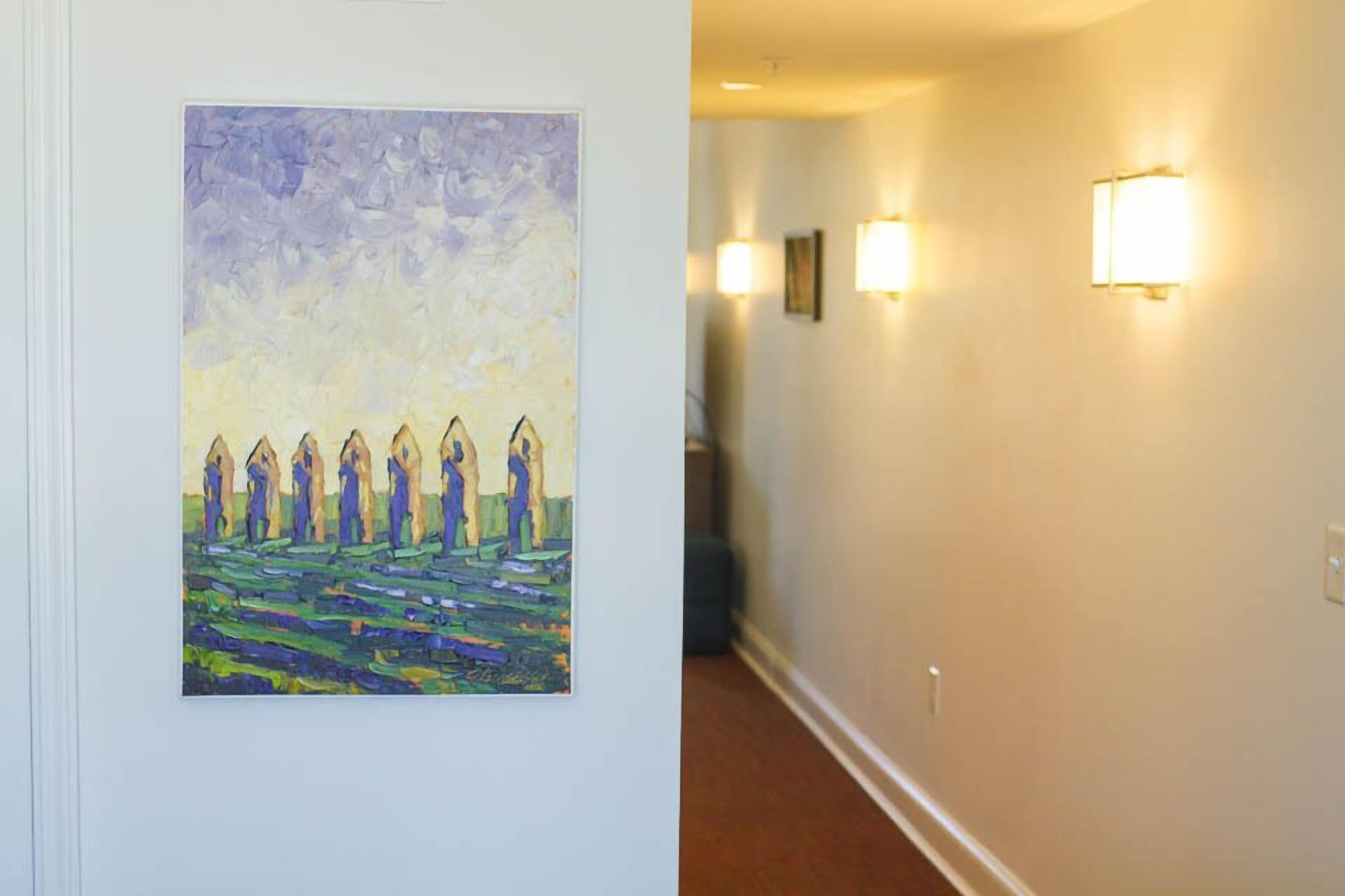 A hallway with a painting on the left wall and wall-mounted lights on the right.
