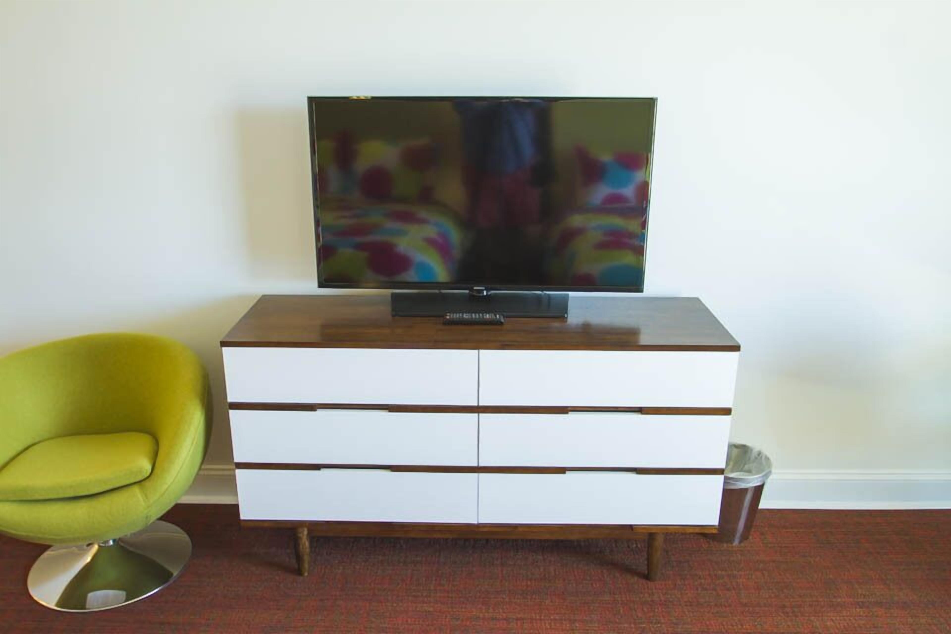 A television on a wooden cabinet with drawers, a green chair, and a carpeted floor.