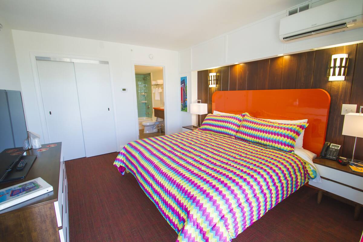A hotel room with a large bed, a desk with a laptop, and a bathroom visible through an open door.