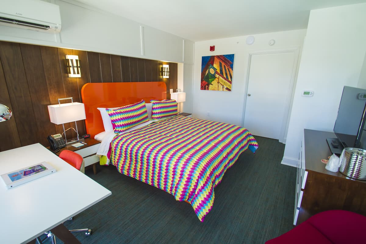 A hotel room with a bed, bedside table, lamp, and a desk with a chair.
