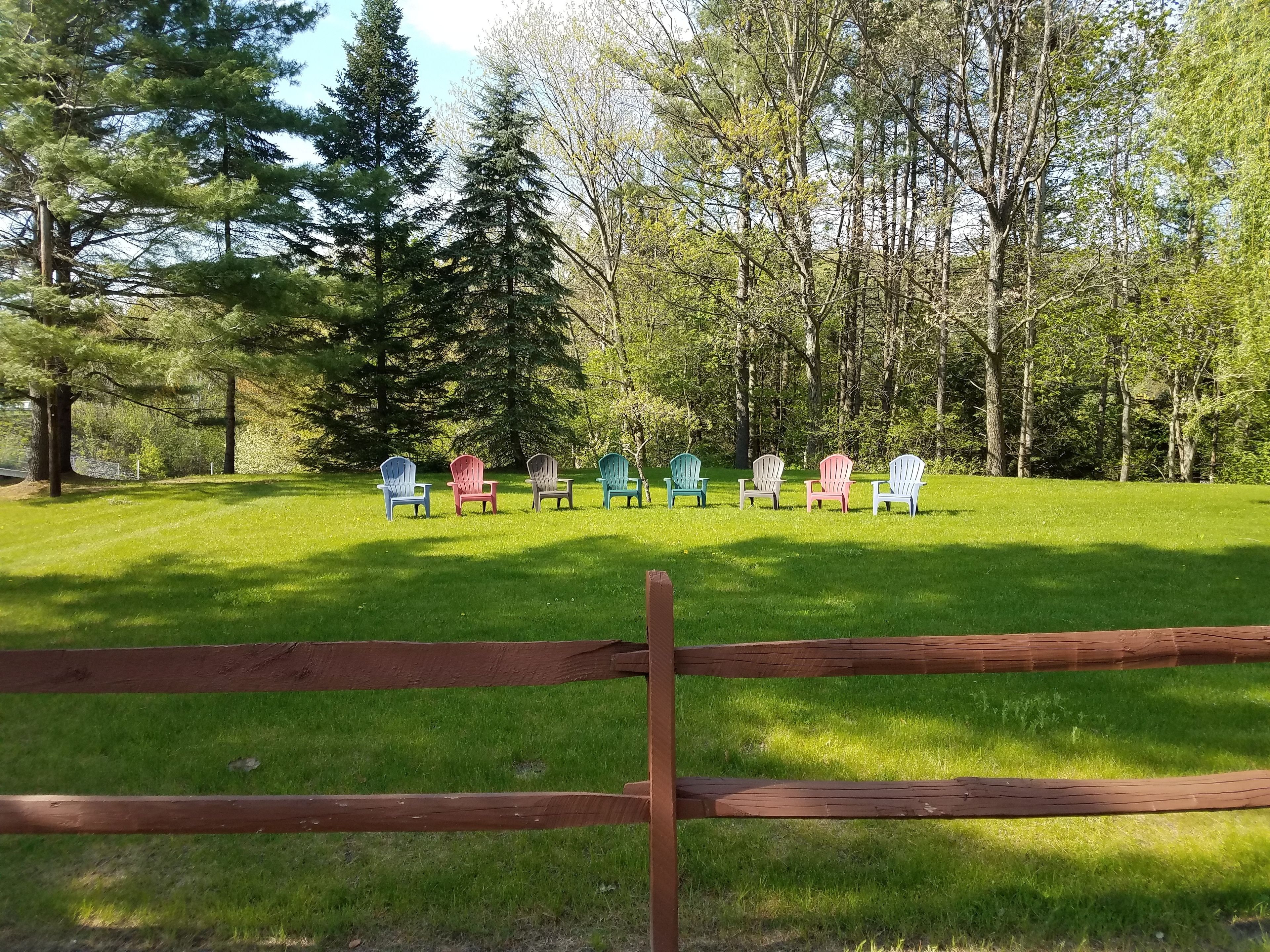 A grassy area with a row of colorful Adirondack chairs and a wooden fence in the foreground.