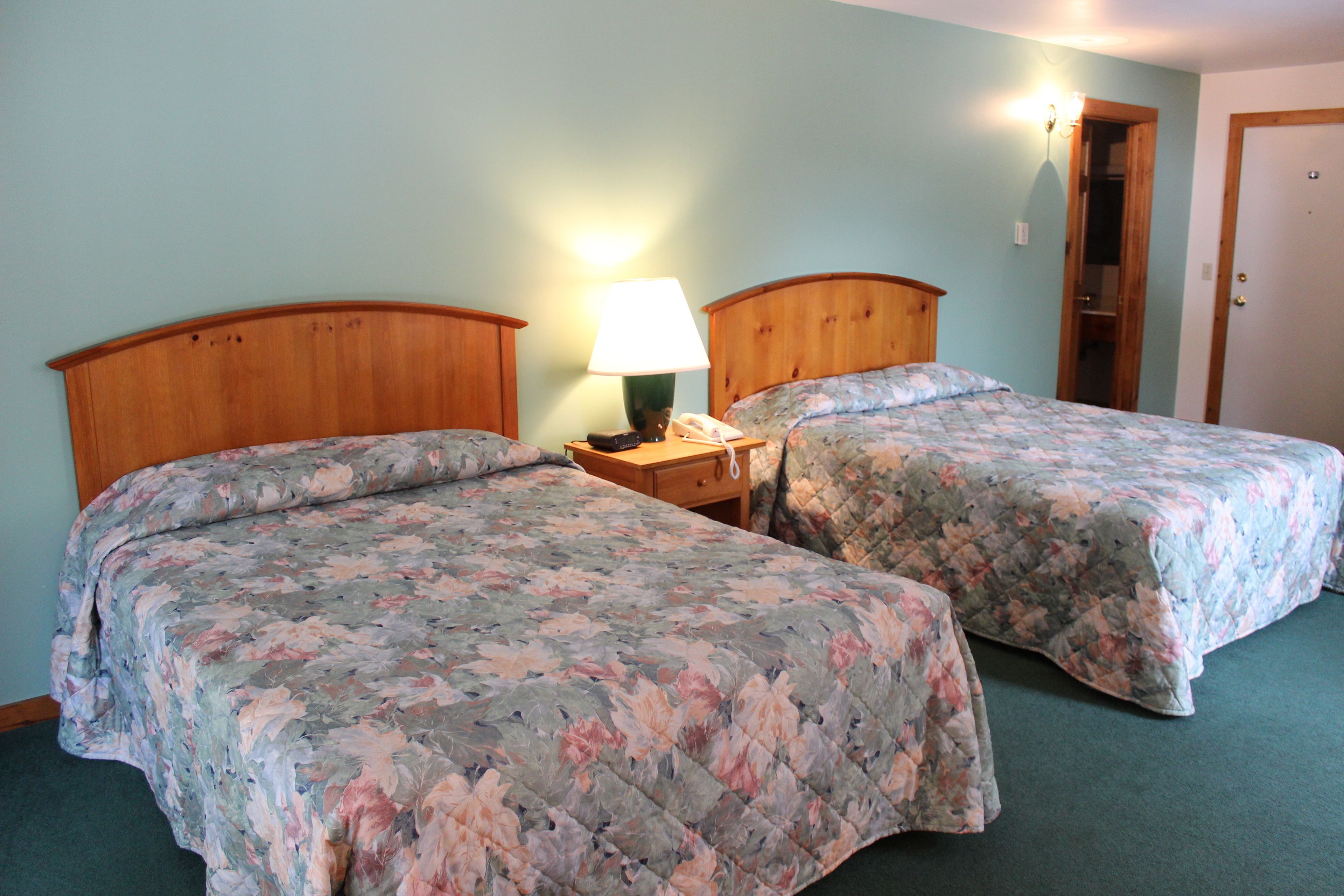 A room with two beds, each with a wooden headboard, a nightstand with a lamp, and a wall-mounted light.