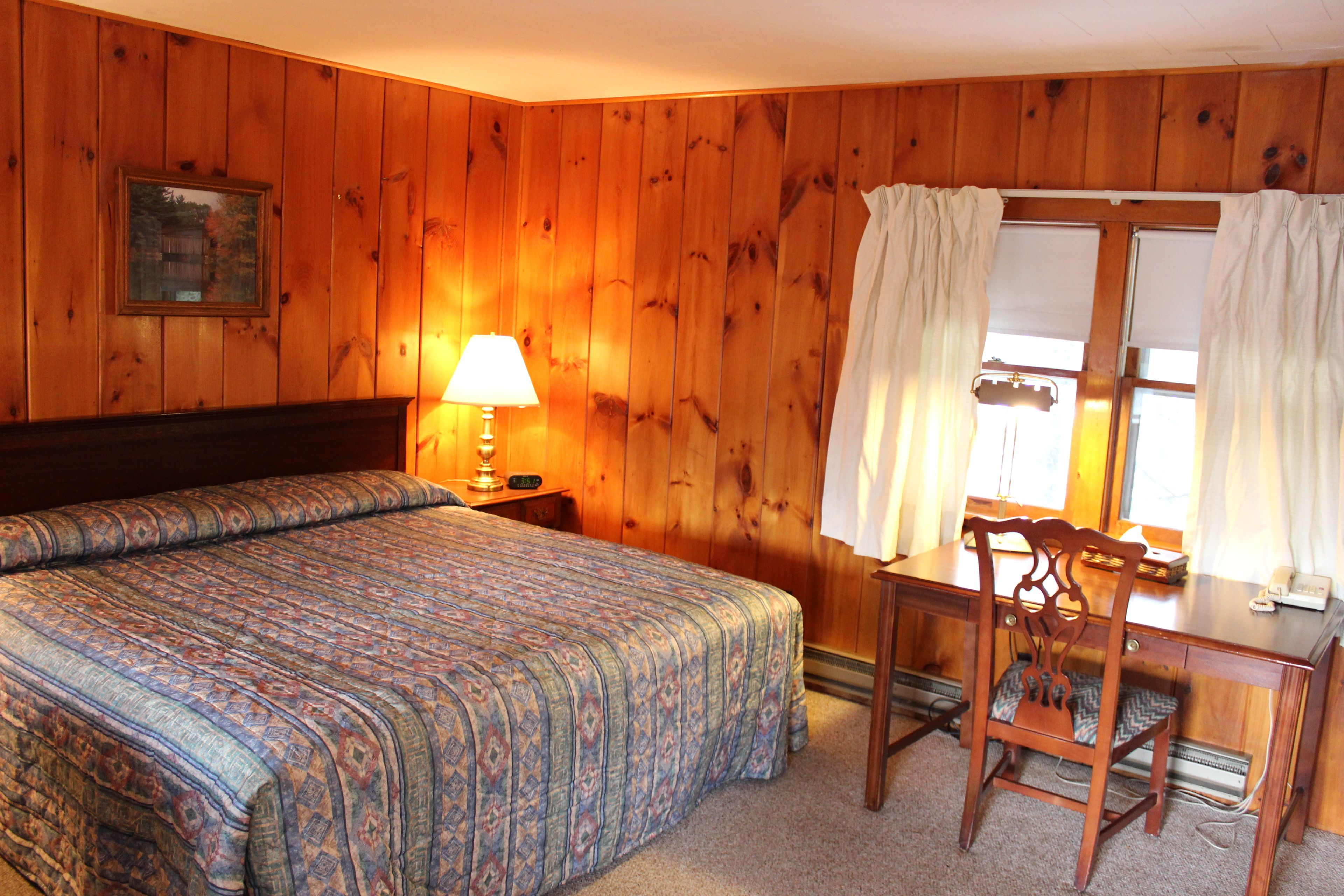 Una habitación con una cama grande, un escritorio de madera y una silla. Hay una lámpara en el escritorio y una ventana con cortinas.