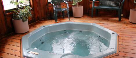 Un jacuzzi en una terraza de madera con plantas en macetas y dos sillas.