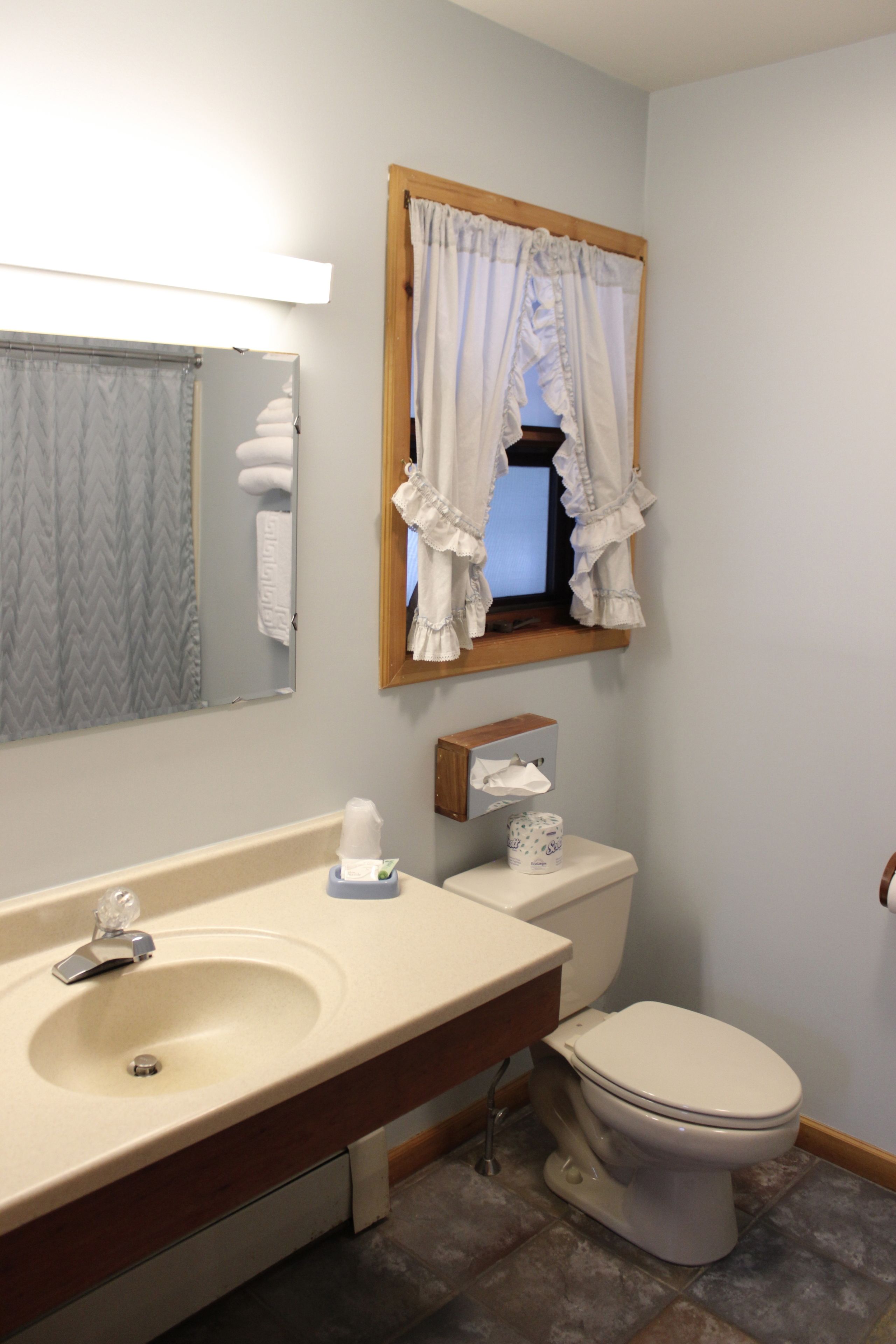 Une salle de bain équipée d’un lavabo, d’un miroir, de toilettes et d’une fenêtre avec des rideaux.