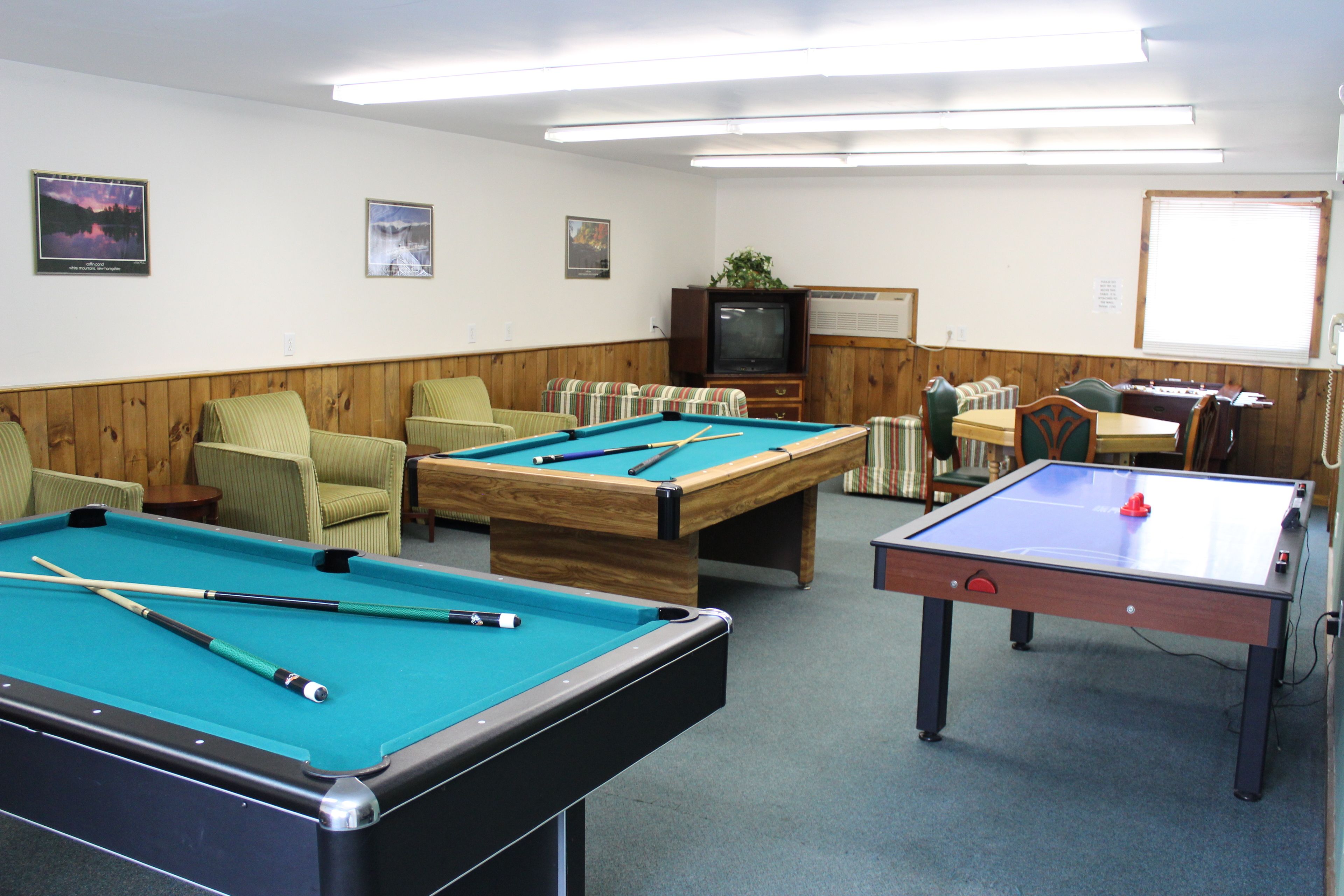 A room with a pool table, a foosball table, and a television.