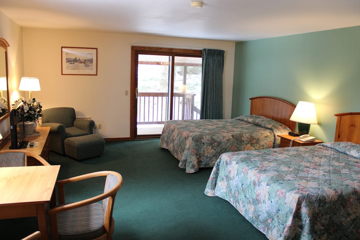 Ein Hotelzimmer mit zwei Betten, einem Schreibtisch mit Stuhl, einem kleinen Tisch und einem Fenster mit Vorhängen.