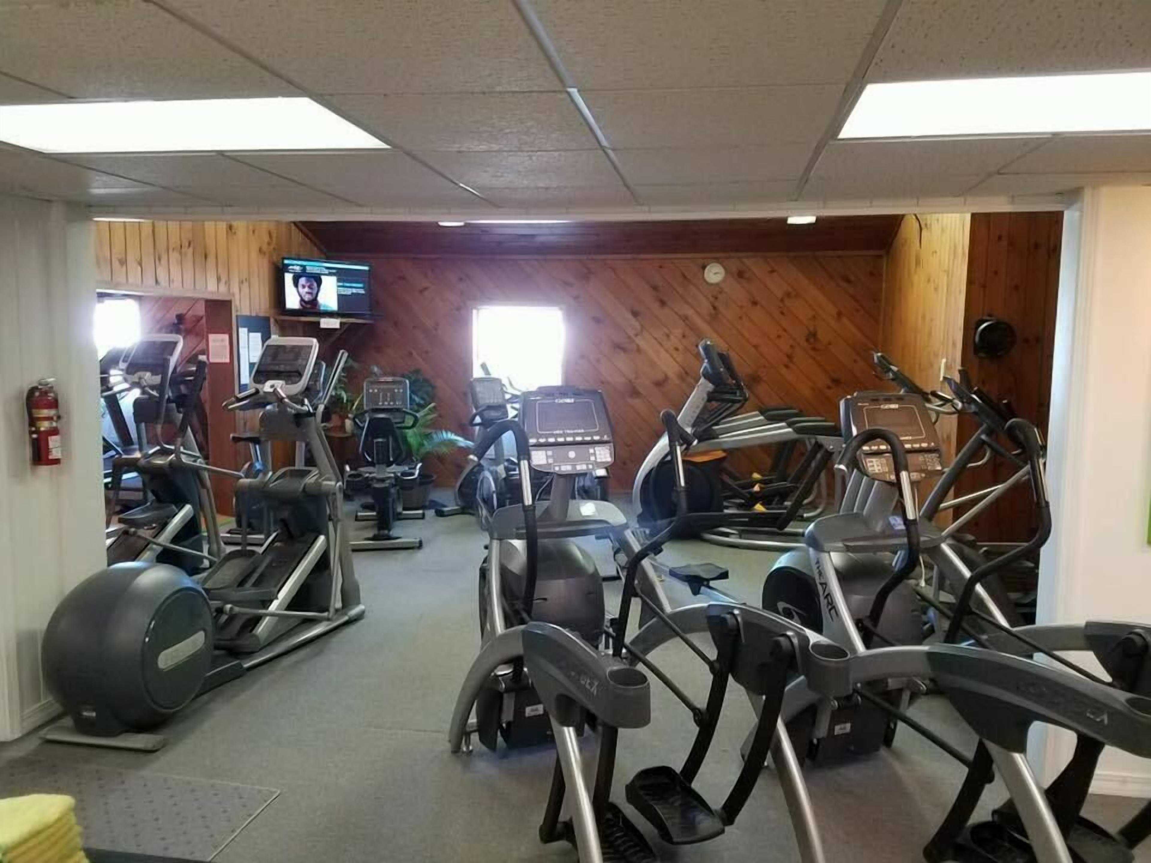 Un gimnasio con varias cintas de correr y máquinas elípticas, paredes de madera y una pantalla de televisión.