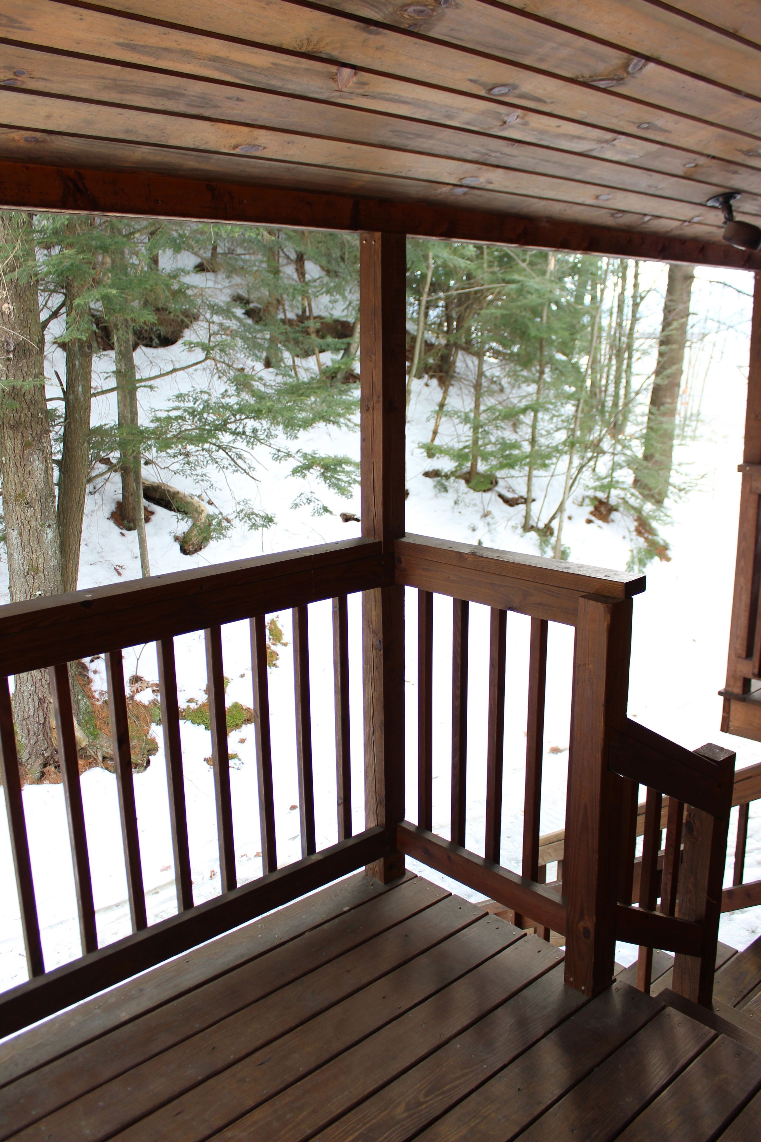 A wooden deck with a railing, overlooking a snowy forest.