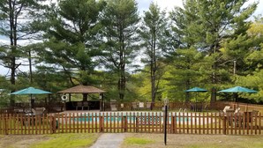 A fenced outdoor area with a pool, picnic tables, and umbrellas.