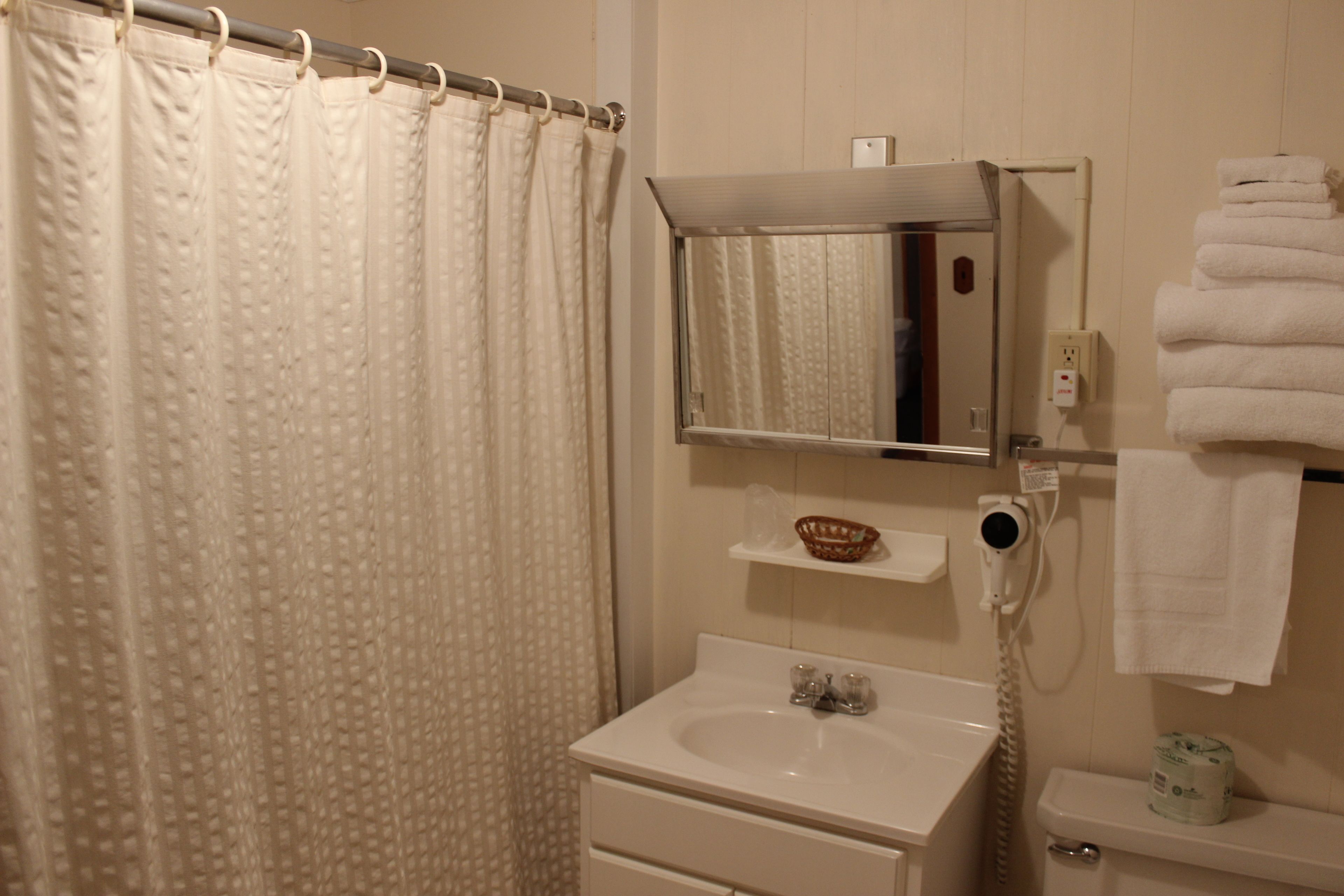 A bathroom with a shower curtain, a sink, a mirror, a towel rack, and a toilet.