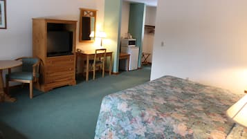 A bedroom with a bed, a desk, a chair, a television, and a microwave.
