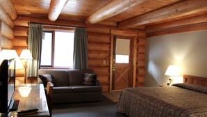 A log cabin room with a bed, a sofa, a desk with a lamp, and a window with curtains.