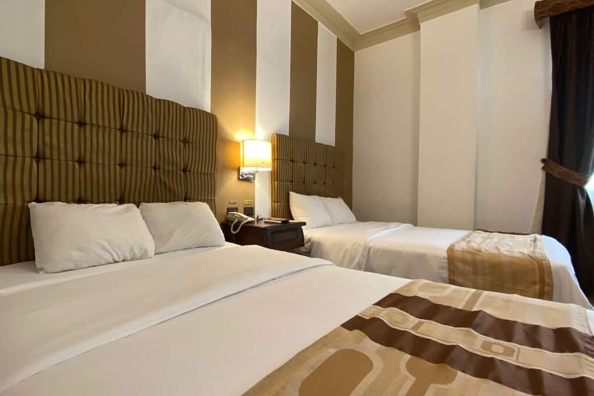 Habitación de hotel con dos camas, cada una con un cabecero a rayas, una mesita de noche con lámpara y teléfono.