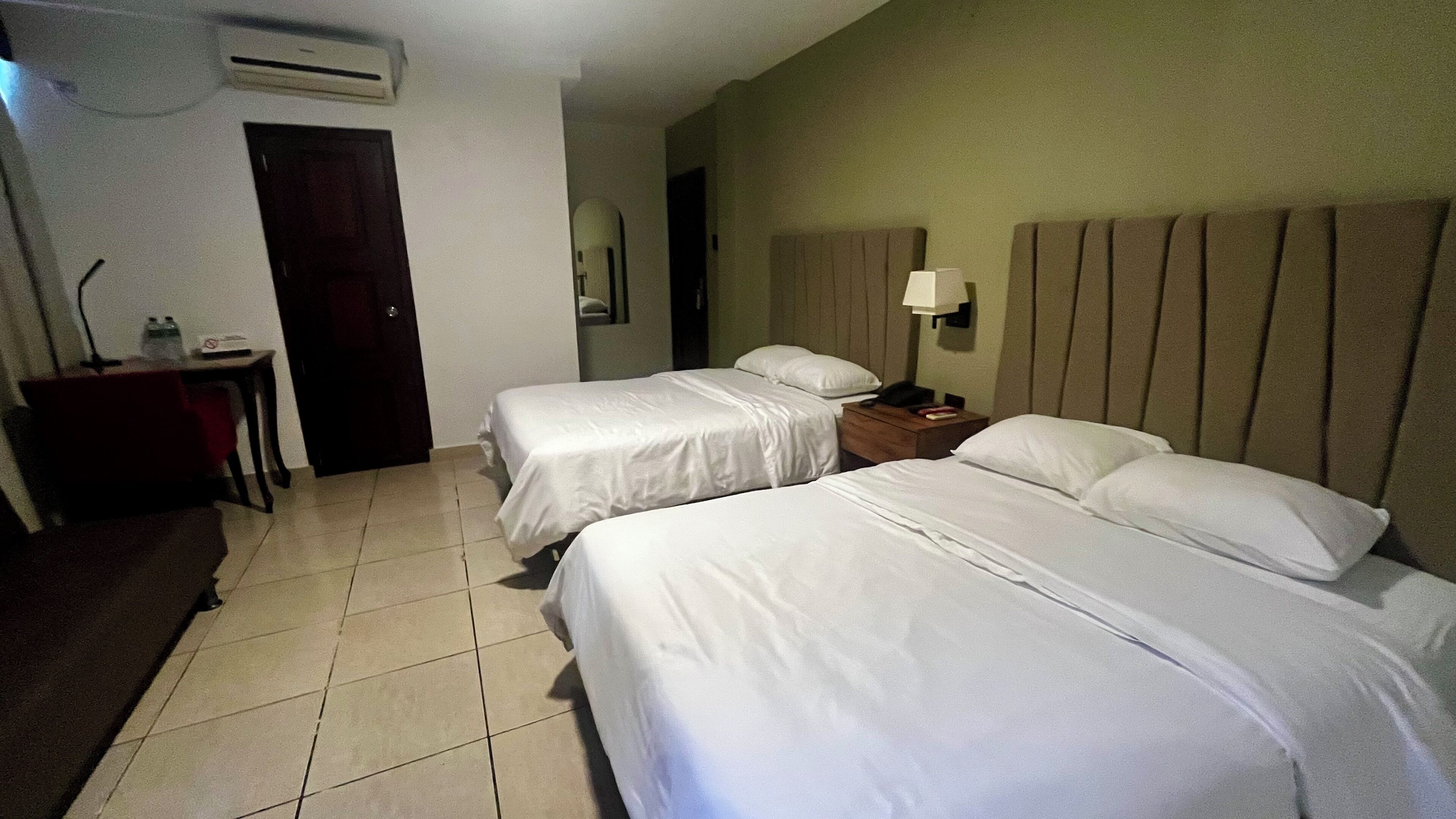 Habitación de hotel con dos camas, un escritorio, una silla, una lámpara y un equipo de aire acondicionado.