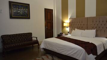 A bedroom with a bed, a sofa, a door, and a wall-mounted lamp.