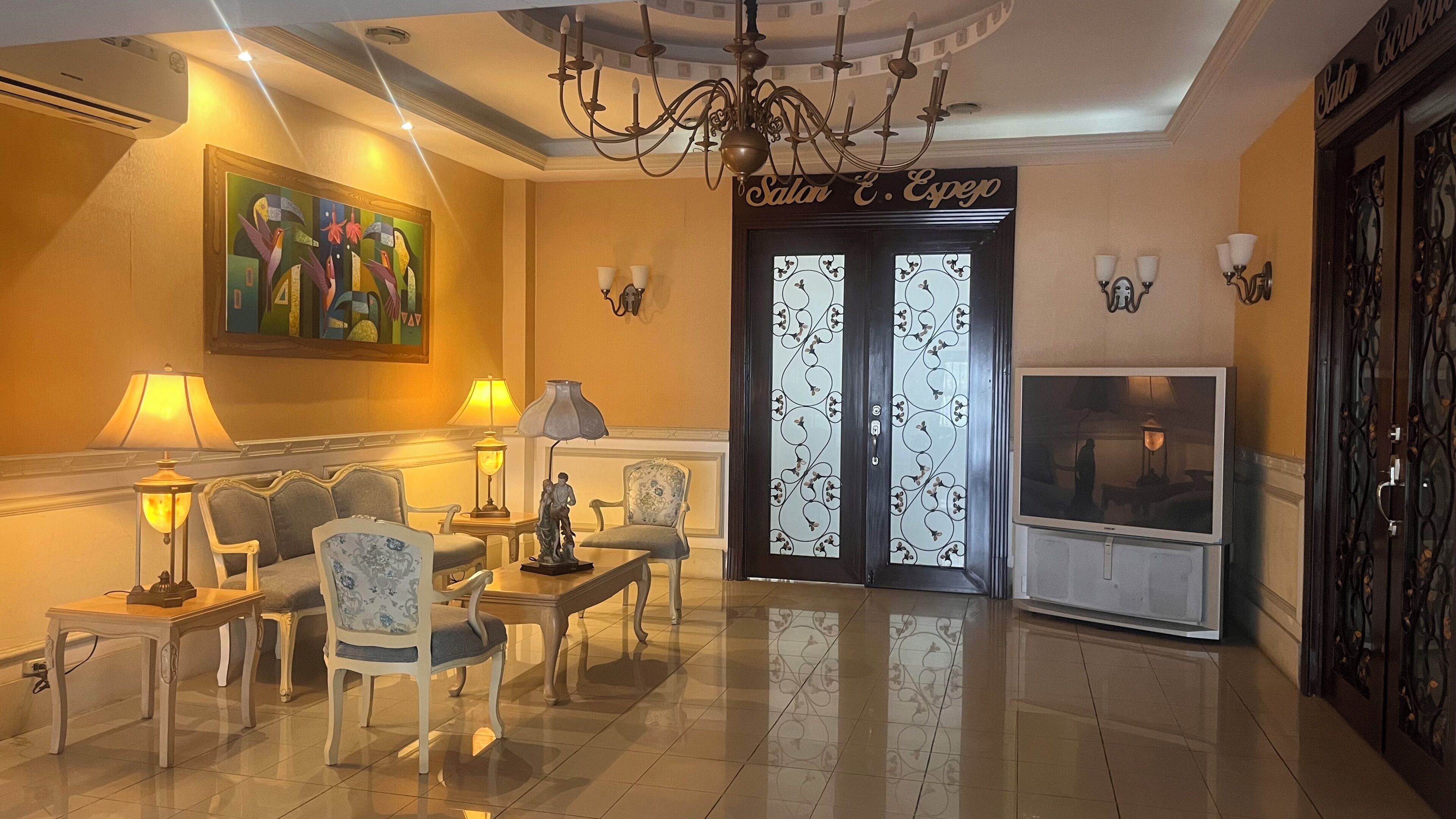 Vestíbulo de hotel con una araña, un cuadro, un mostrador de recepción y un televisor.