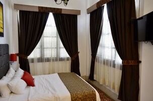 A hotel room with a bed, curtains, a TV, and a window with blinds.