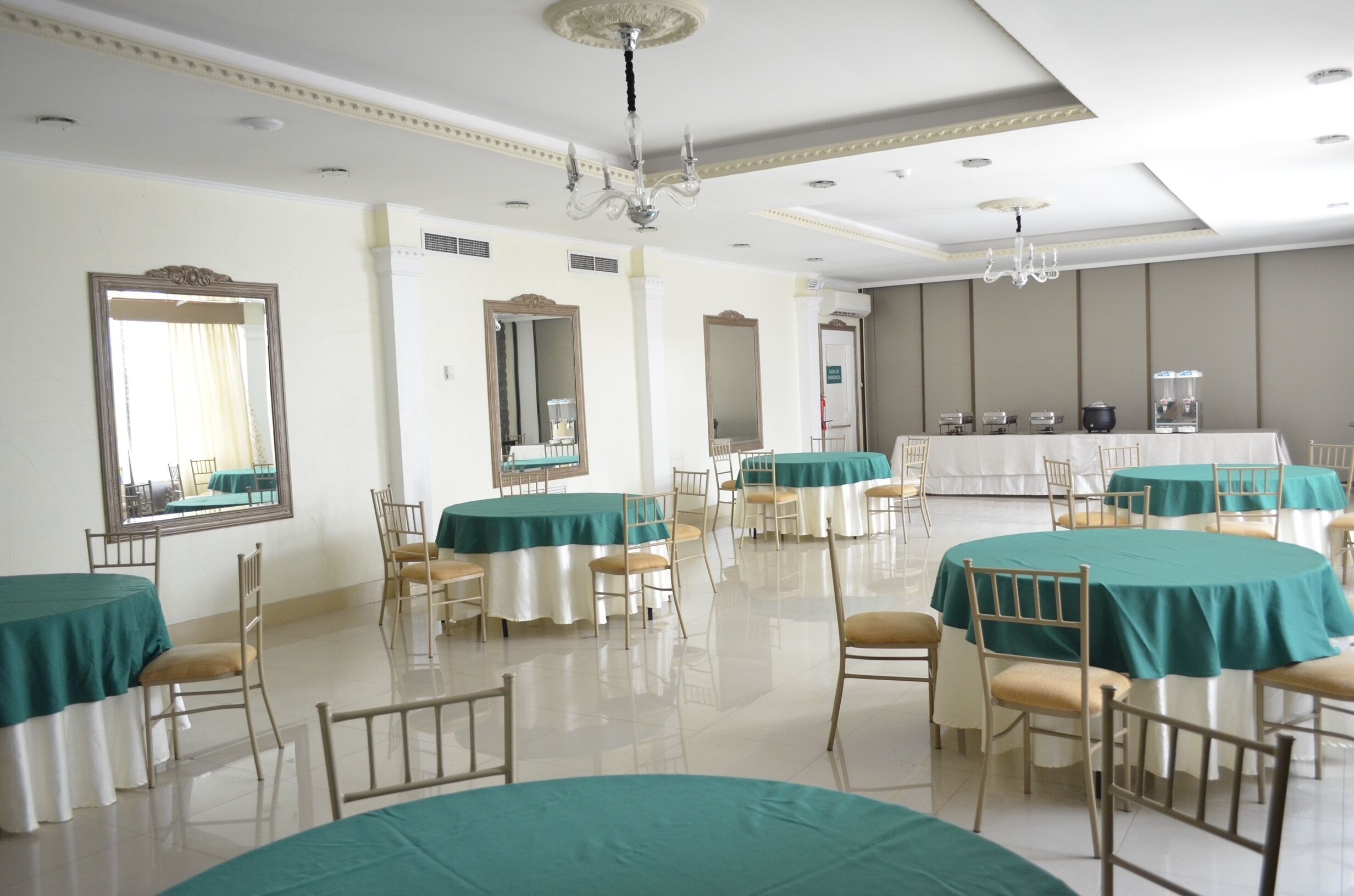 Een restaurant in een hotel, met ronde tafels bedekt met teal tafelkleden, houten stoelen en een kroonluchter.
