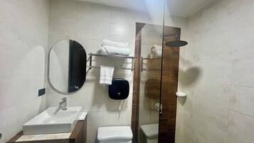 Un baño moderno con ducha de vidrio, espejo redondo, lavabo e inodoro.