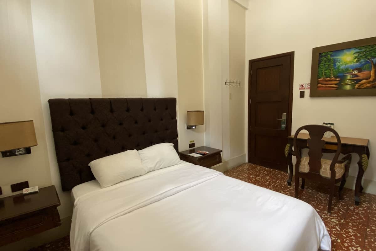 Una habitación de hotel con una cama grande, un escritorio, una silla, una puerta y un cuadro en la pared.