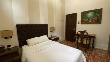 Quarto de hotel com uma cama grande, uma escrivaninha, uma cadeira, uma porta e um quadro na parede.