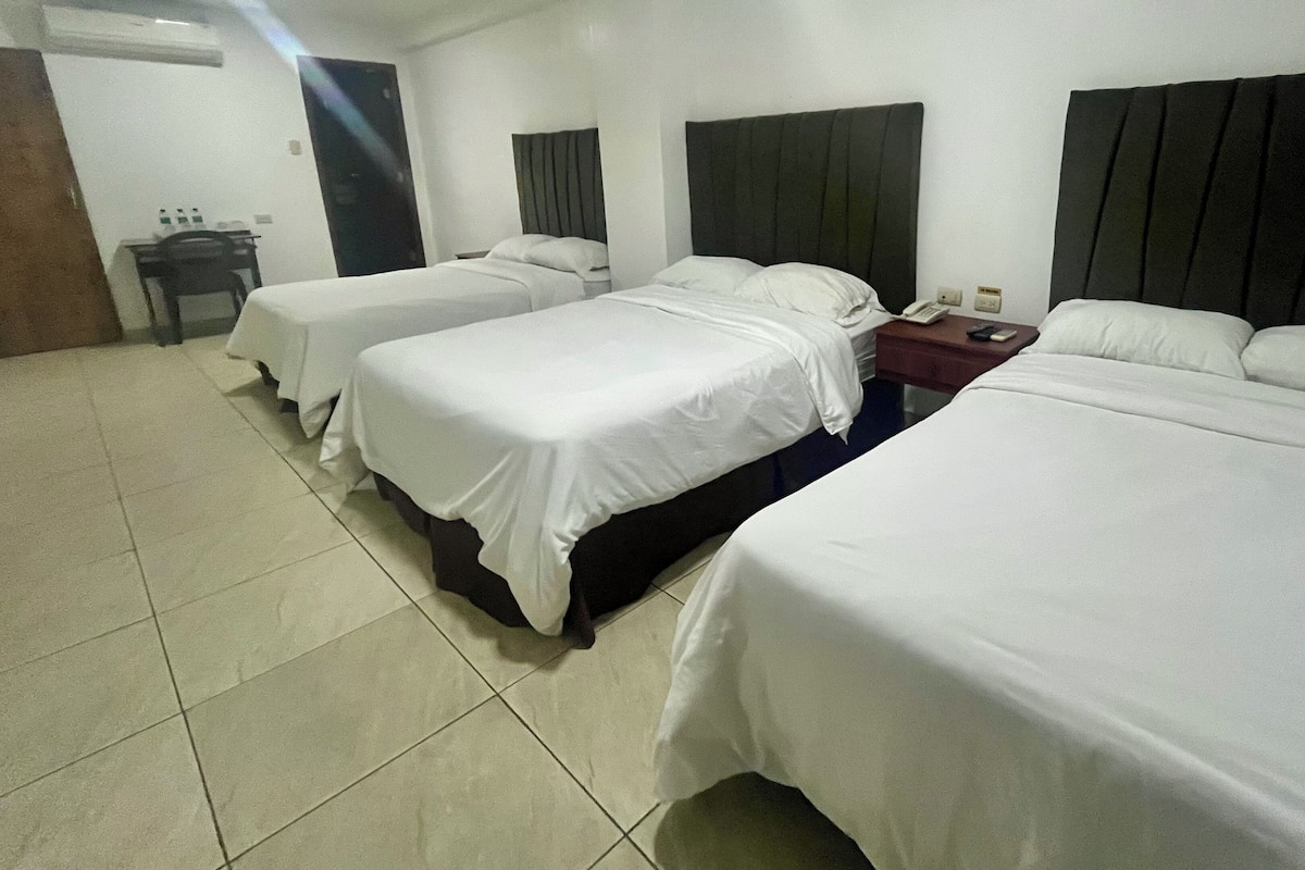 Una habitación de hotel con tres camas, un escritorio y una silla.