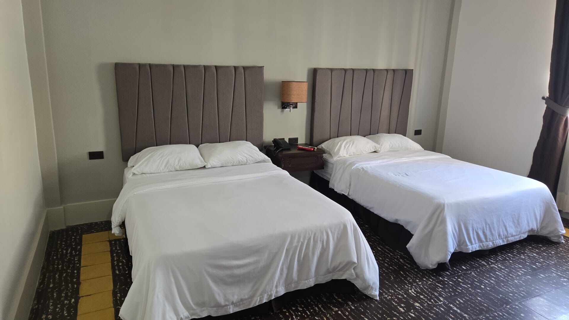 Een hotelkamer met twee enkele bedden, een nachtkastje met een lamp en een telefoon.
