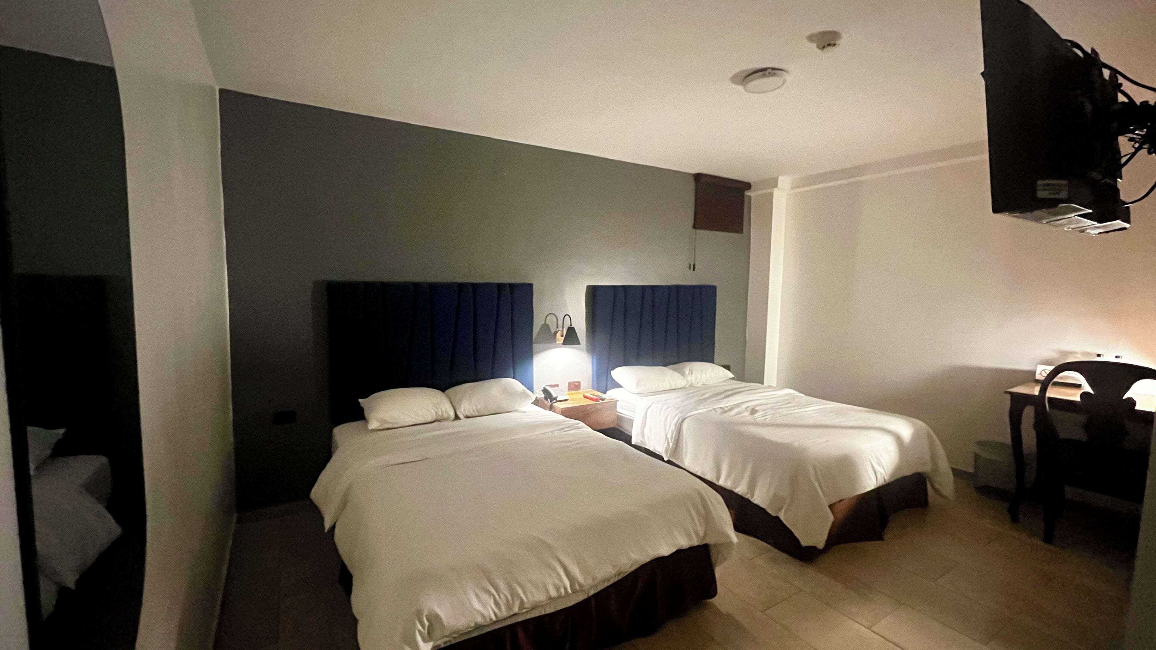 A hotel room with two beds, a desk, a chair, and a television.