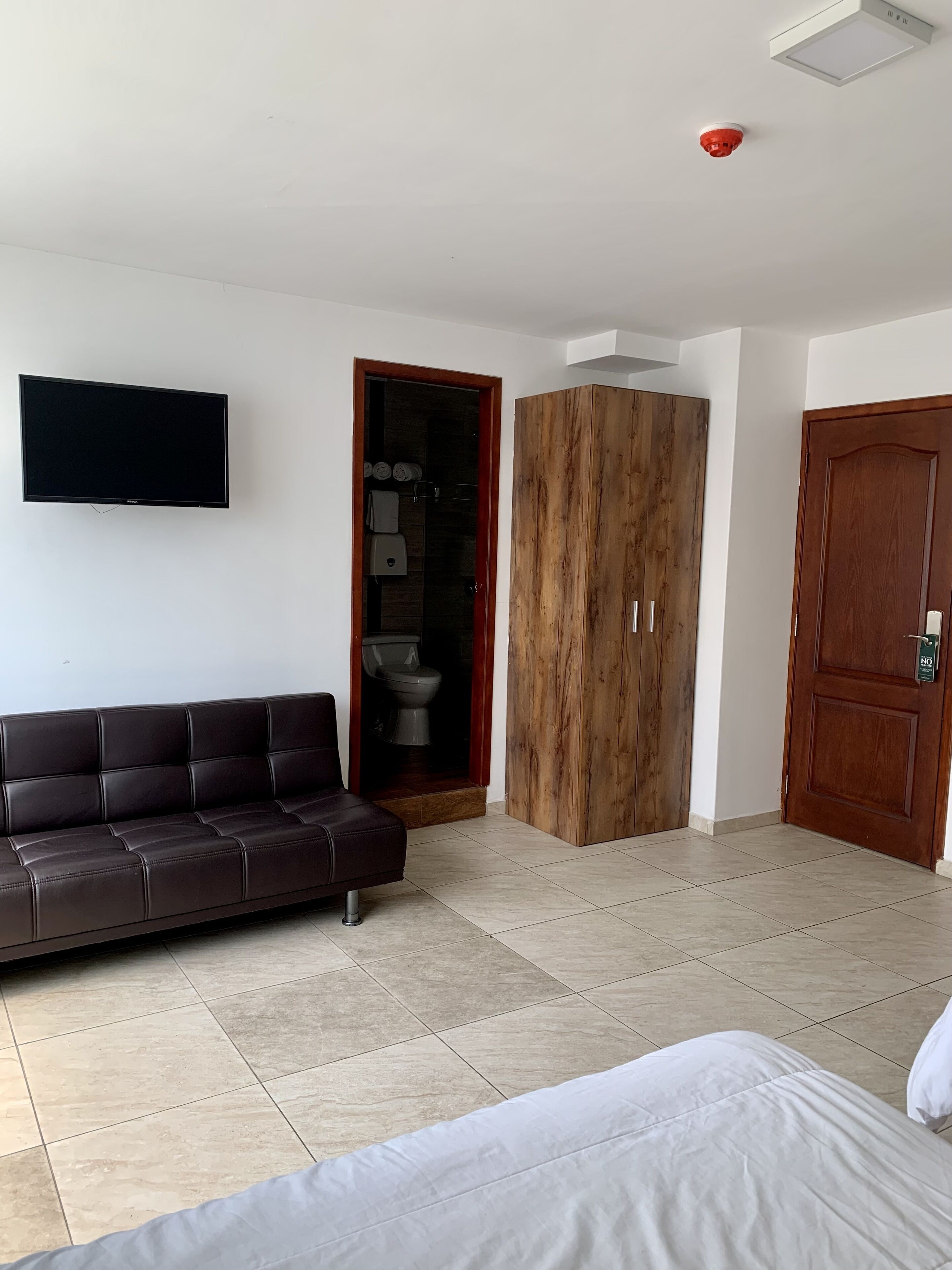 Une chambre moderne équipée d’un téléviseur à écran plat, d’un canapé en cuir marron foncé, d’une armoire en bois et d’une porte en bois.