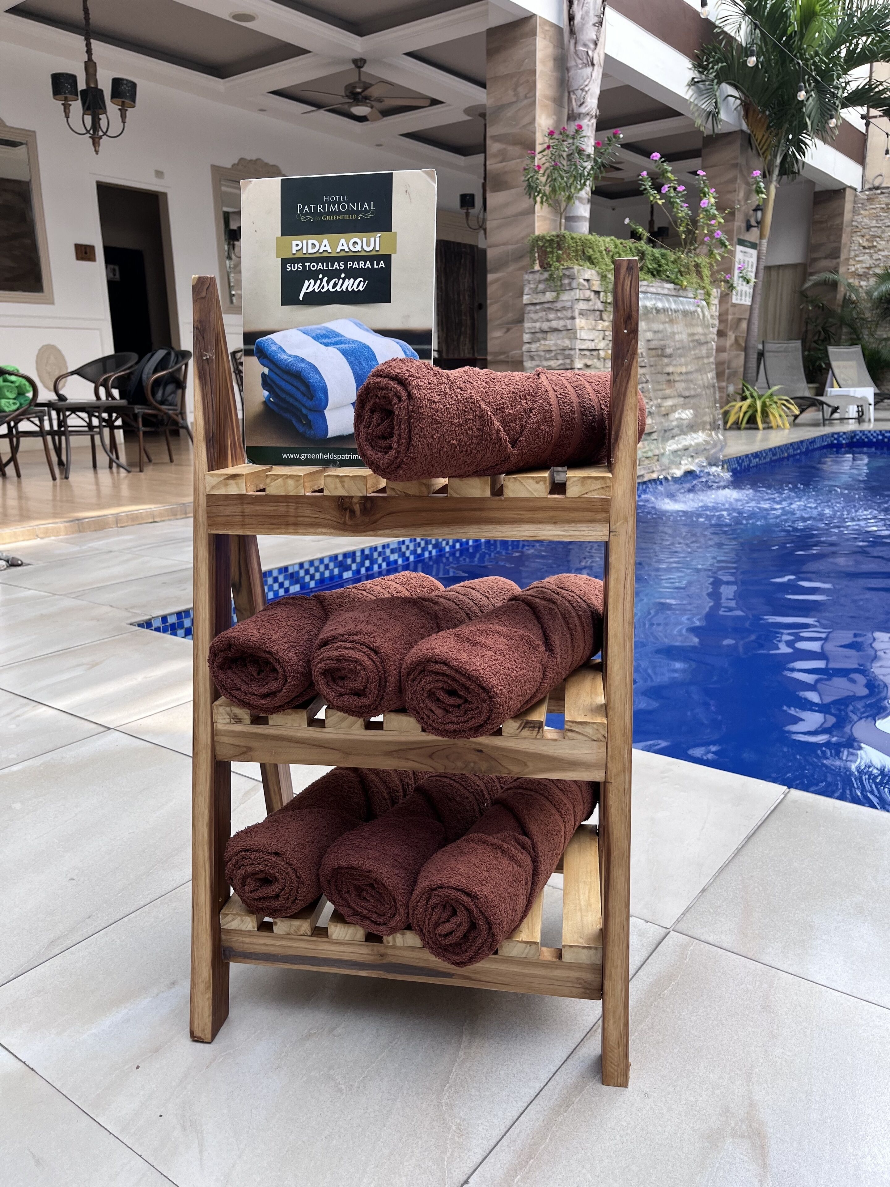 Un porte-serviettes en bois avec plusieurs serviettes marron, une enseigne indiquant «Hôtel PATRIMONIAL», et une piscine en arrière-plan.
