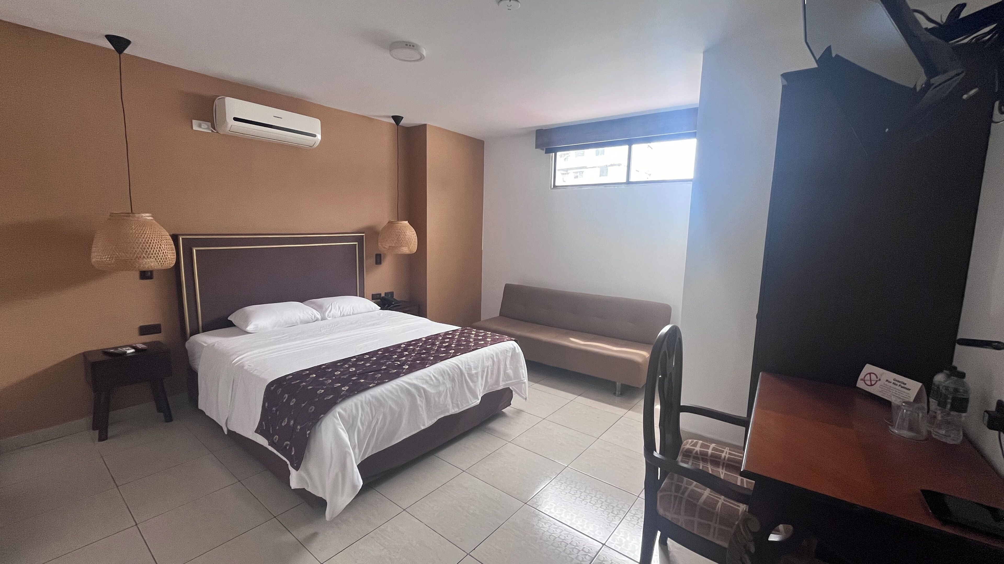 Une chambre d’hôtel comprenant un lit, un canapé, un bureau avec une chaise, un climatiseur et une fenêtre.