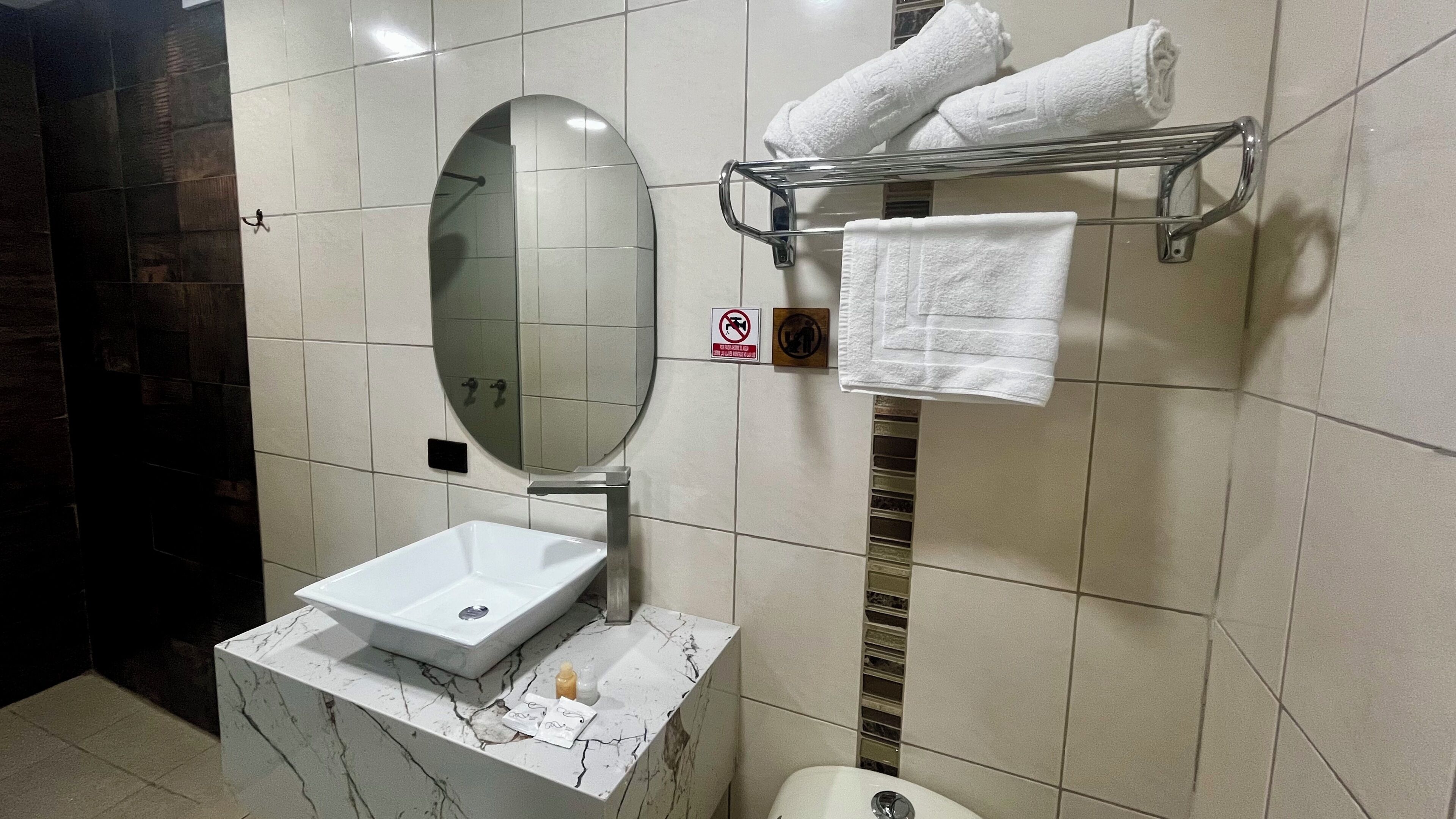 A bathroom with a white sink, a mirror, a towel rack with towels, and a no-smoking sign.