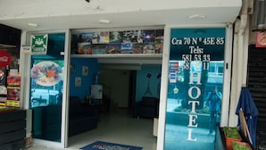 L’entrée d’un hôtel avec un comptoir d’accueil, un mur bleu orné de photos et un numéro de téléphone bien visible.