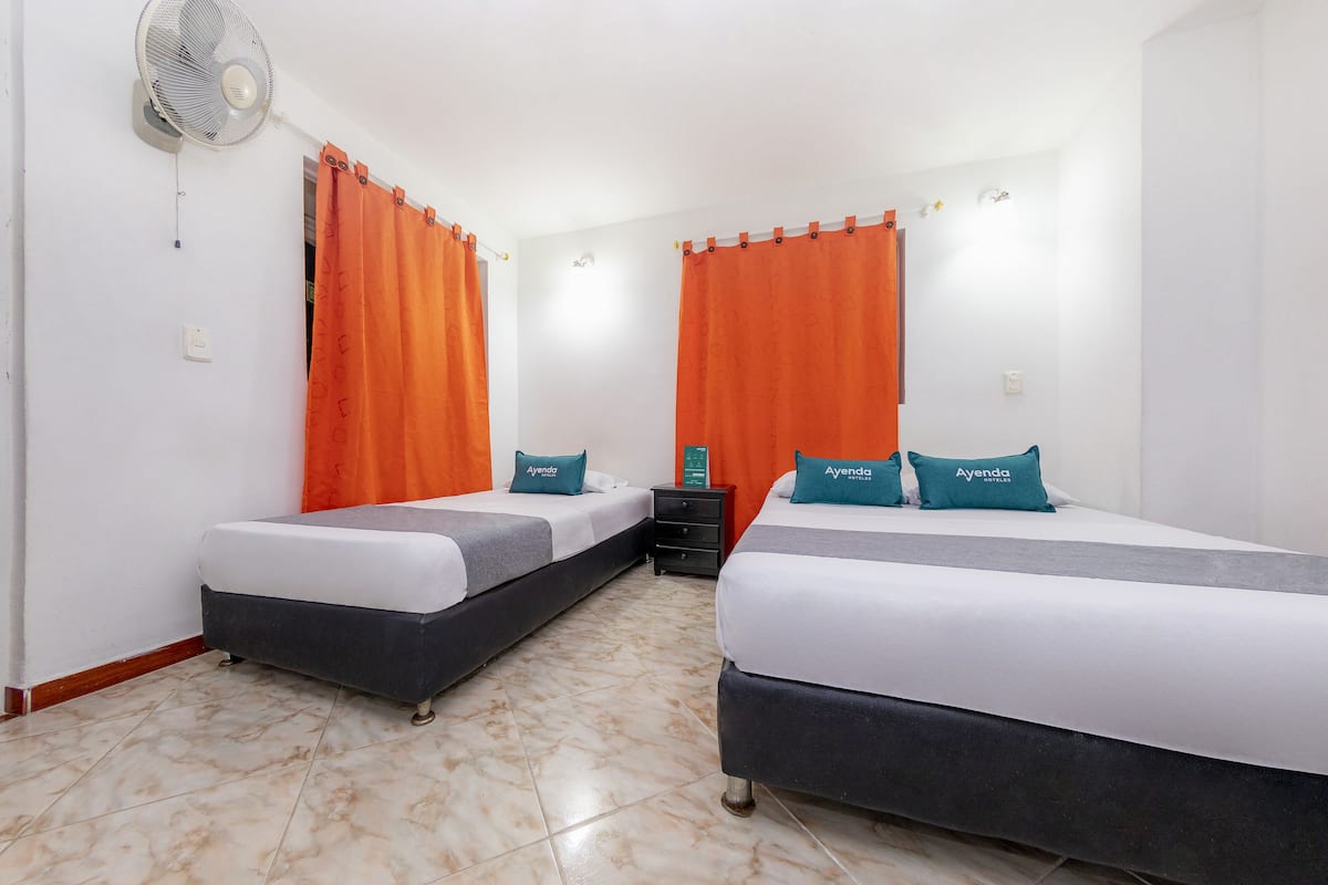 Habitación de hotel con dos camas, cortinas naranjas, un ventilador y una mesita de noche.