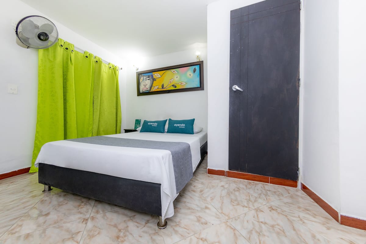 Una habitación de hotel con una cama, cortinas verdes, un cuadro y una puerta.