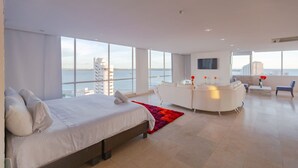 A modern hotel room with a large bed, a sitting area, and a view of the sea. - Hotel La Gran Via (Bocagrande)