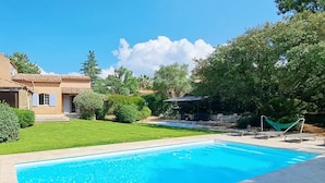 A swimming pool with a clear blue water, surrounded by a well-maintained lawn and a house with a tiled roof. - Villa Dourmidou · Heated pool · Bandol wine region · Near beaches (La Cadière-D'azur)