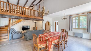 A spacious living room with a dining table, wooden chairs, a sofa, and a staircase leading to an upper level. - Villa Dourmidou · Heated pool · Bandol wine region · Near beaches (La Cadière-D'azur)